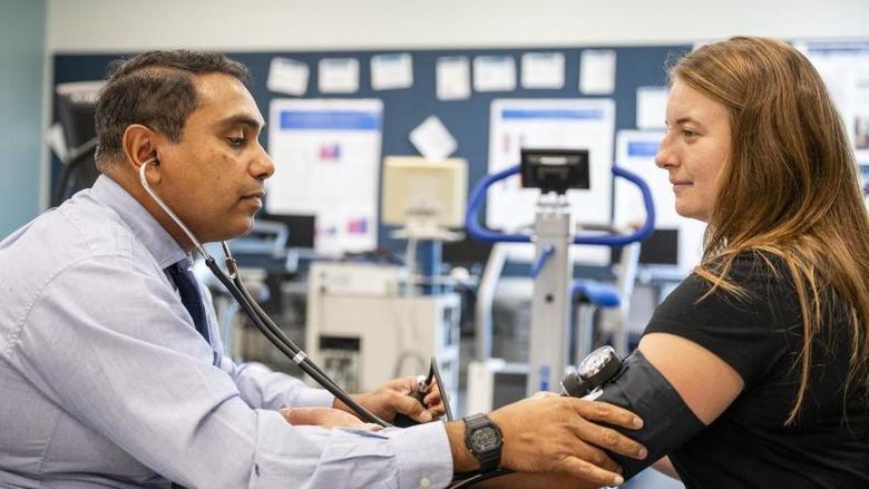 One person wearing a stethoscope takes the blood pressure of another person